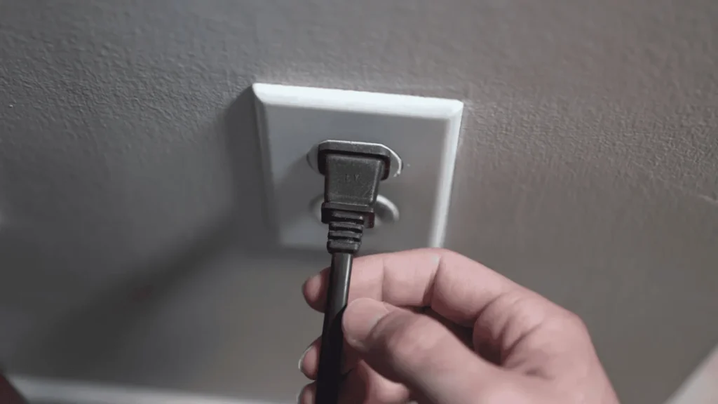 Hand unplugging the power cord of an Onn TV from the wall outlet.