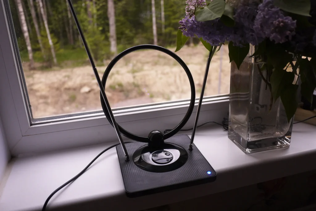 Person adjusting indoor TV antenna near window.