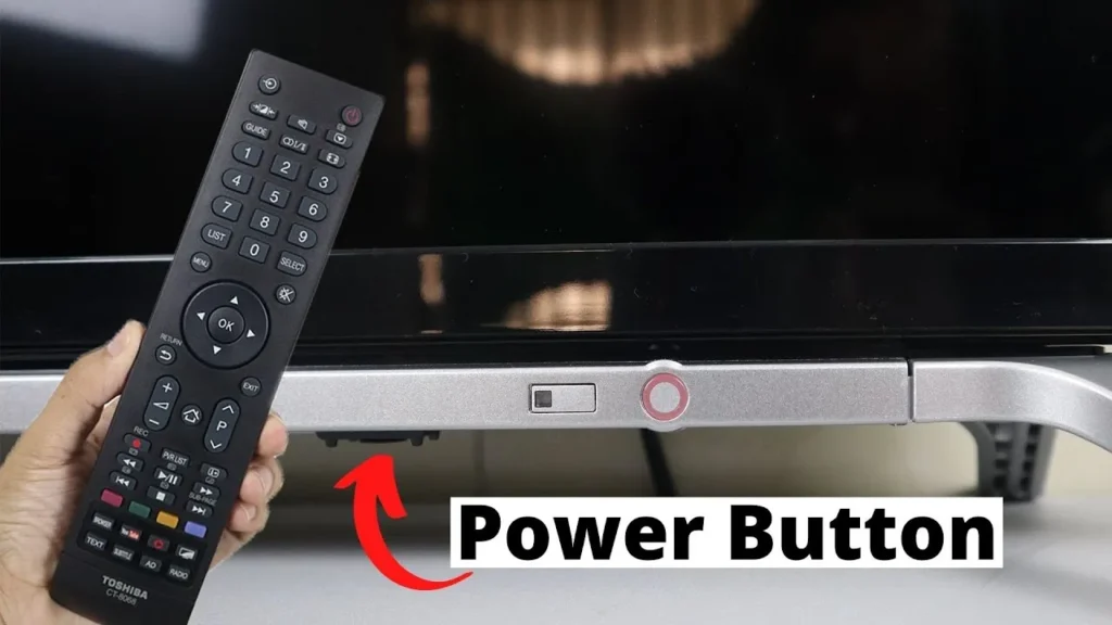 Hand pressing the power button located on the bottom of a Toshiba TV.